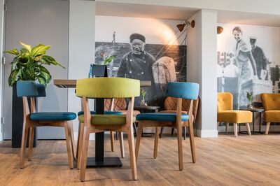 Kleurrijke stoelen rond een houten tafel in een moderne inrichting met muurschilderingen van mensen.